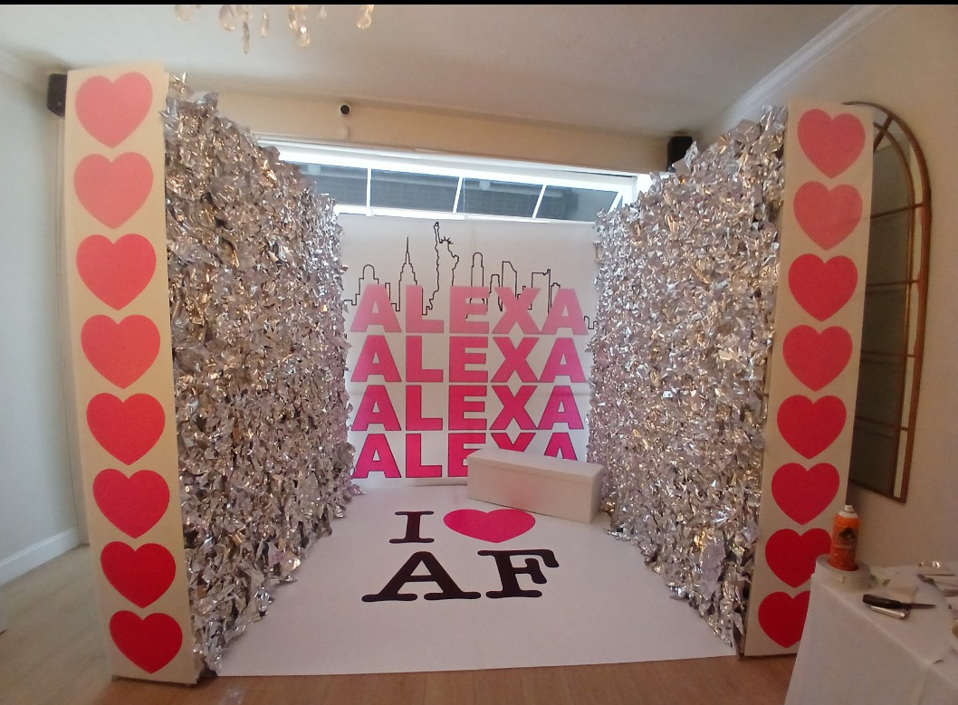 Pink hearts border foil walls flanking a backdrop reading 