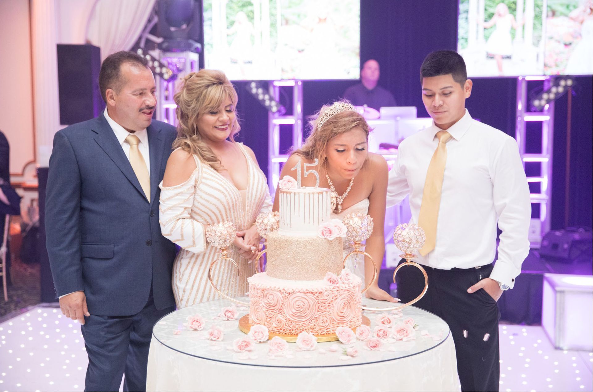 Family celebrating; girl blowing out candles on a three-tiered cake at a party.