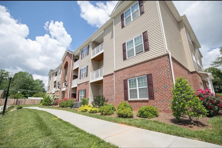Apartment building with brick and beige siding, a walkway, and a blue sky.