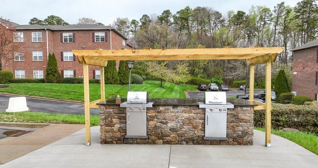 Outdoor barbecue station with two grills, stone base, wooden pergola, in front of apartments.