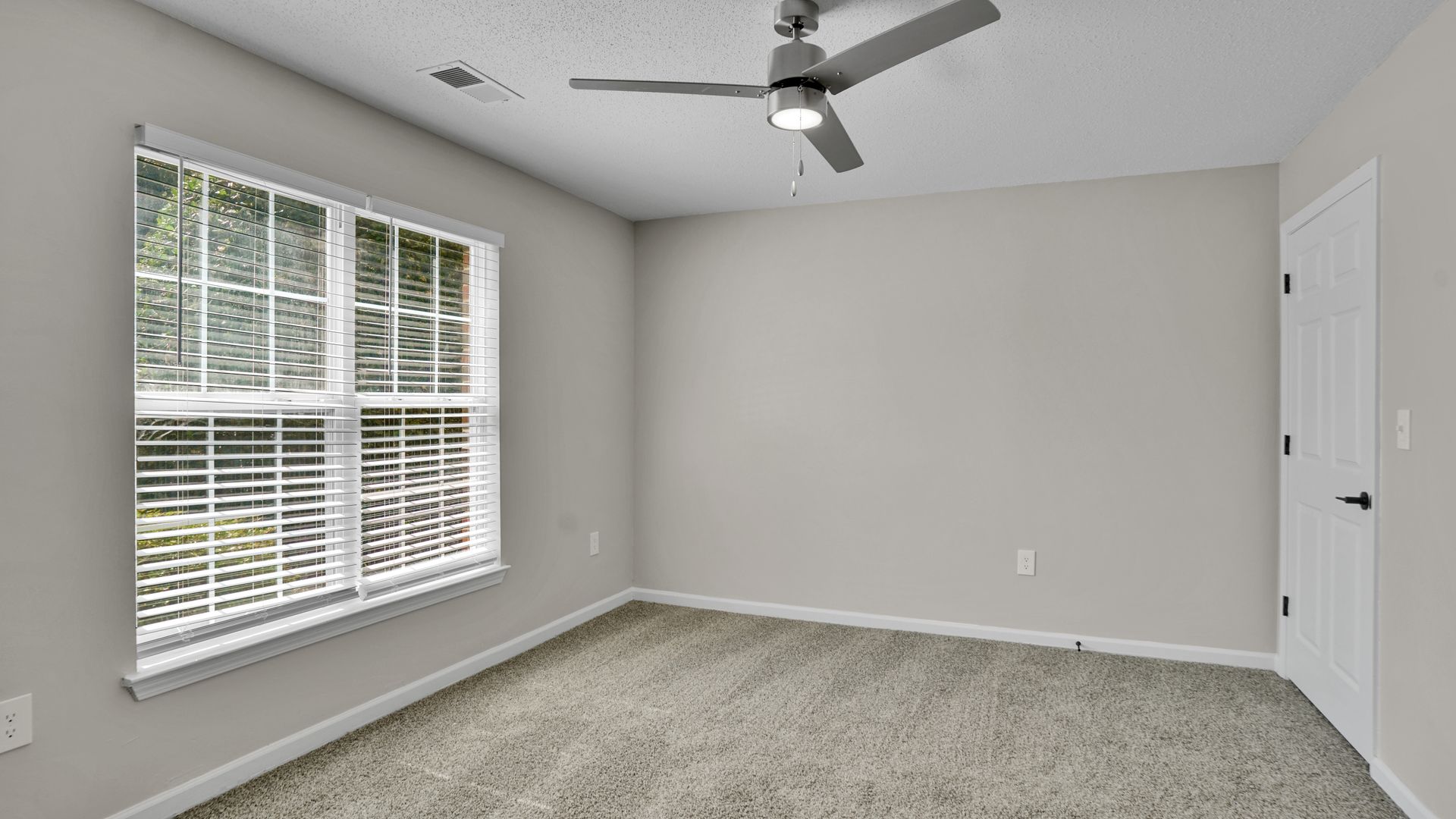An empty room with a ceiling fan and sliding glass doors at Lynx Gate City in Greensboro, NC.