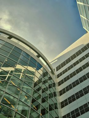 Curved glass office building and tall tower against a cloudy sky, viewed from below