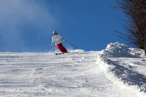 Skier in red pants carving down a snowy slope under a clear blue sky.