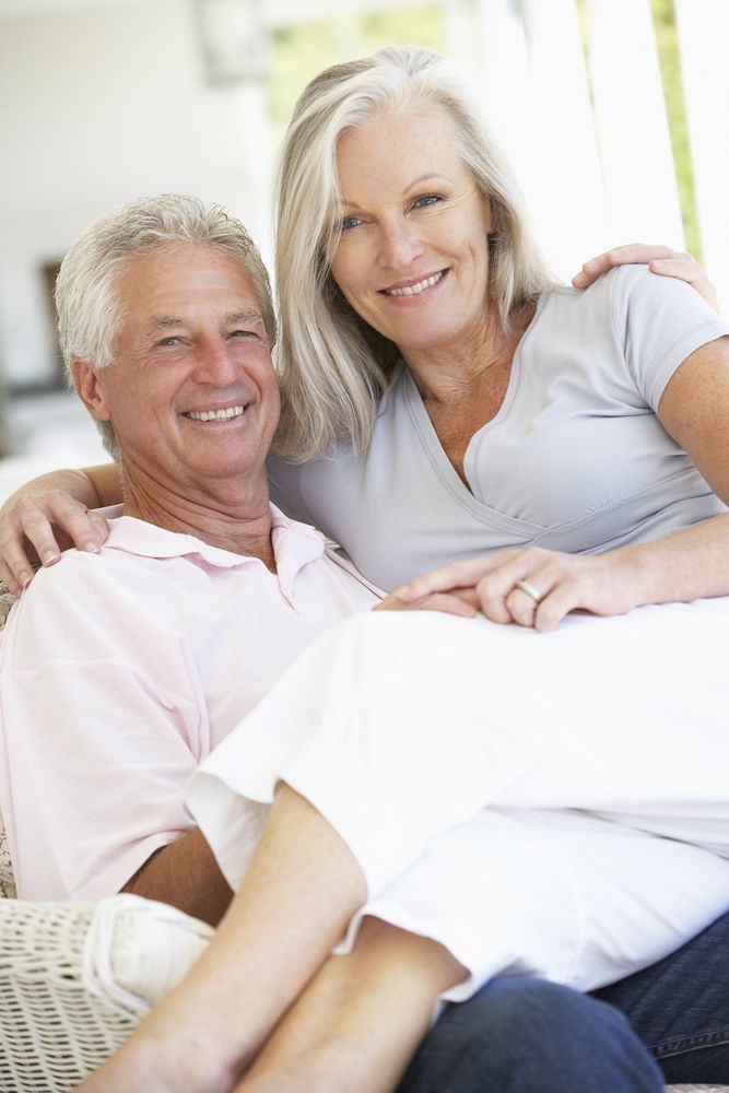 An older man and a woman are sitting on a couch and smiling.