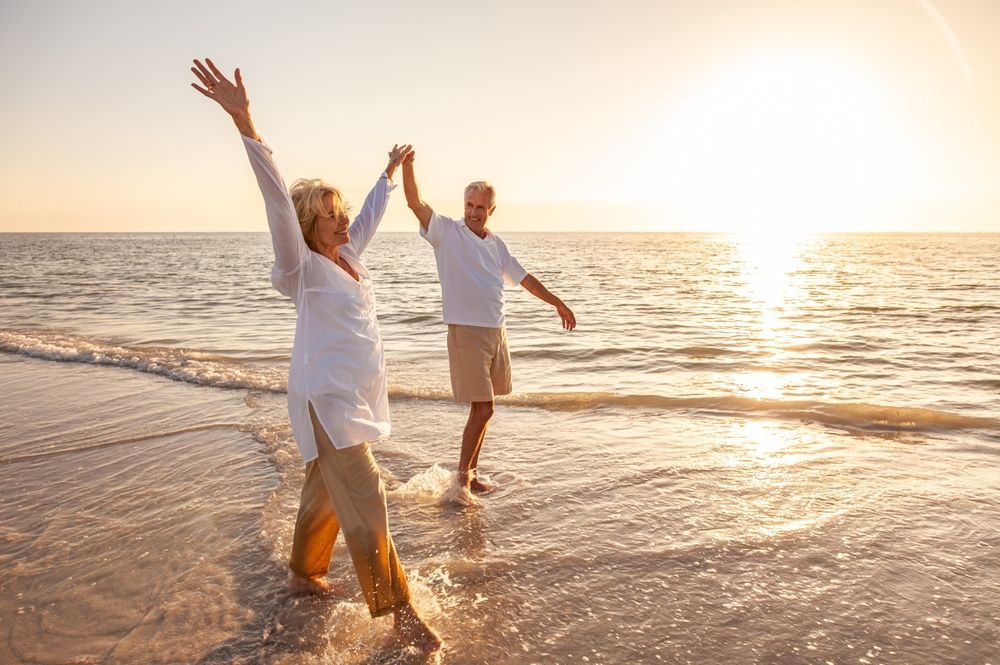 An elderly couple is dancing on the beach at sunset.