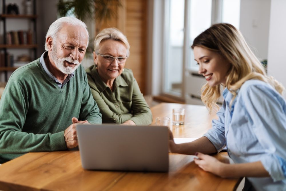 A woman is sitting at a table with two older people looking at a laptop computer.