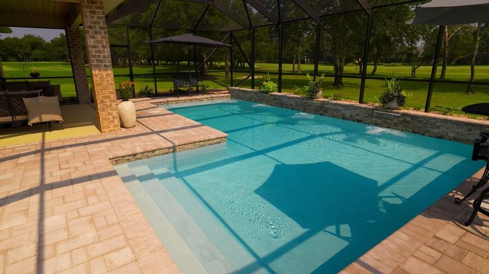 A large swimming pool is surrounded by a screened in area and a patio.