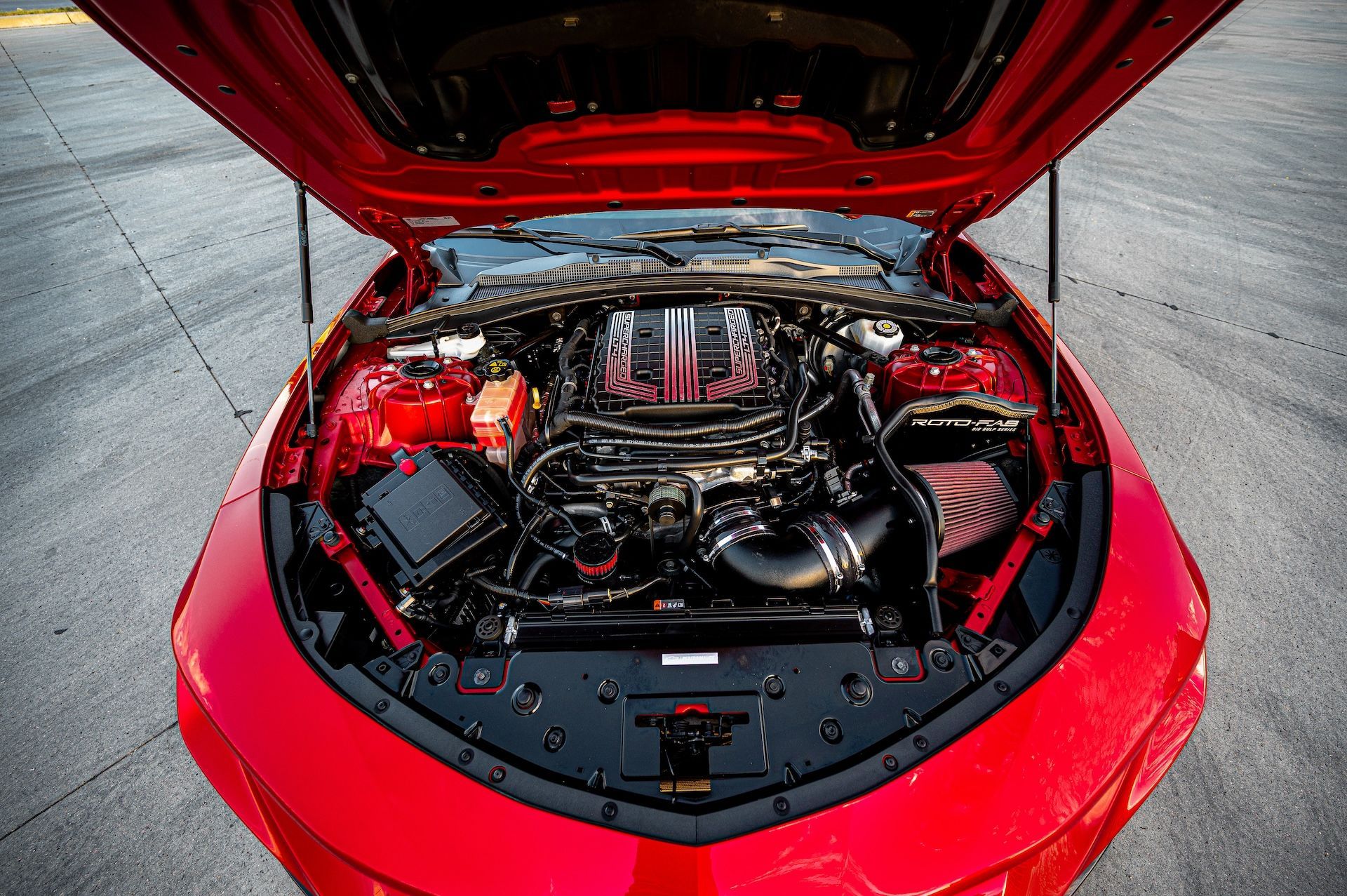 The engine of a red car is shown with the hood open.