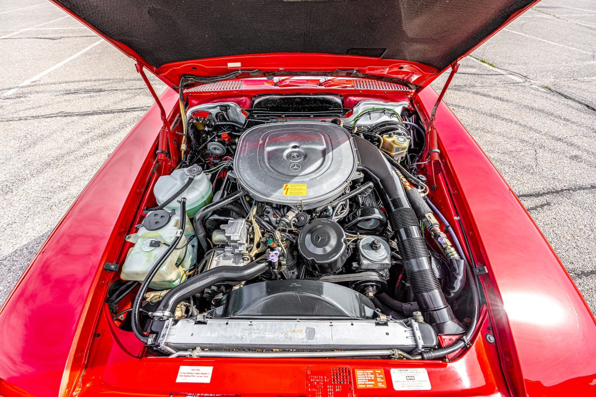 The engine of a red car is shown with the hood open.