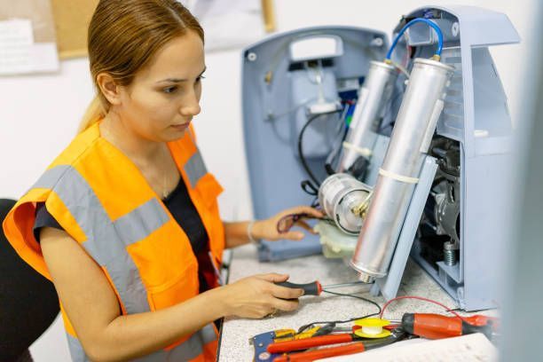 Woman in safety vest repairs equipment using tools.