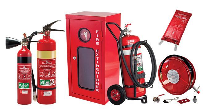 Fire safety technician inspects red fire extinguishers in a facility, wearing blue coveralls and gloves.