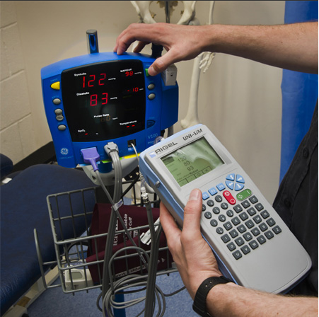 Hands in blue gloves use a multimeter to test the internal components of a medical device.
