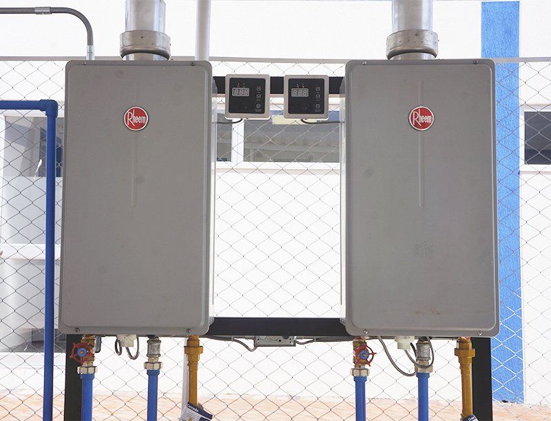 Dos calentadores de agua están ubicados uno al lado del otro encima de una cerca de alambre de cadena.