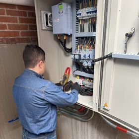 Un hombre con una camisa azul está trabajando en una caja eléctrica.