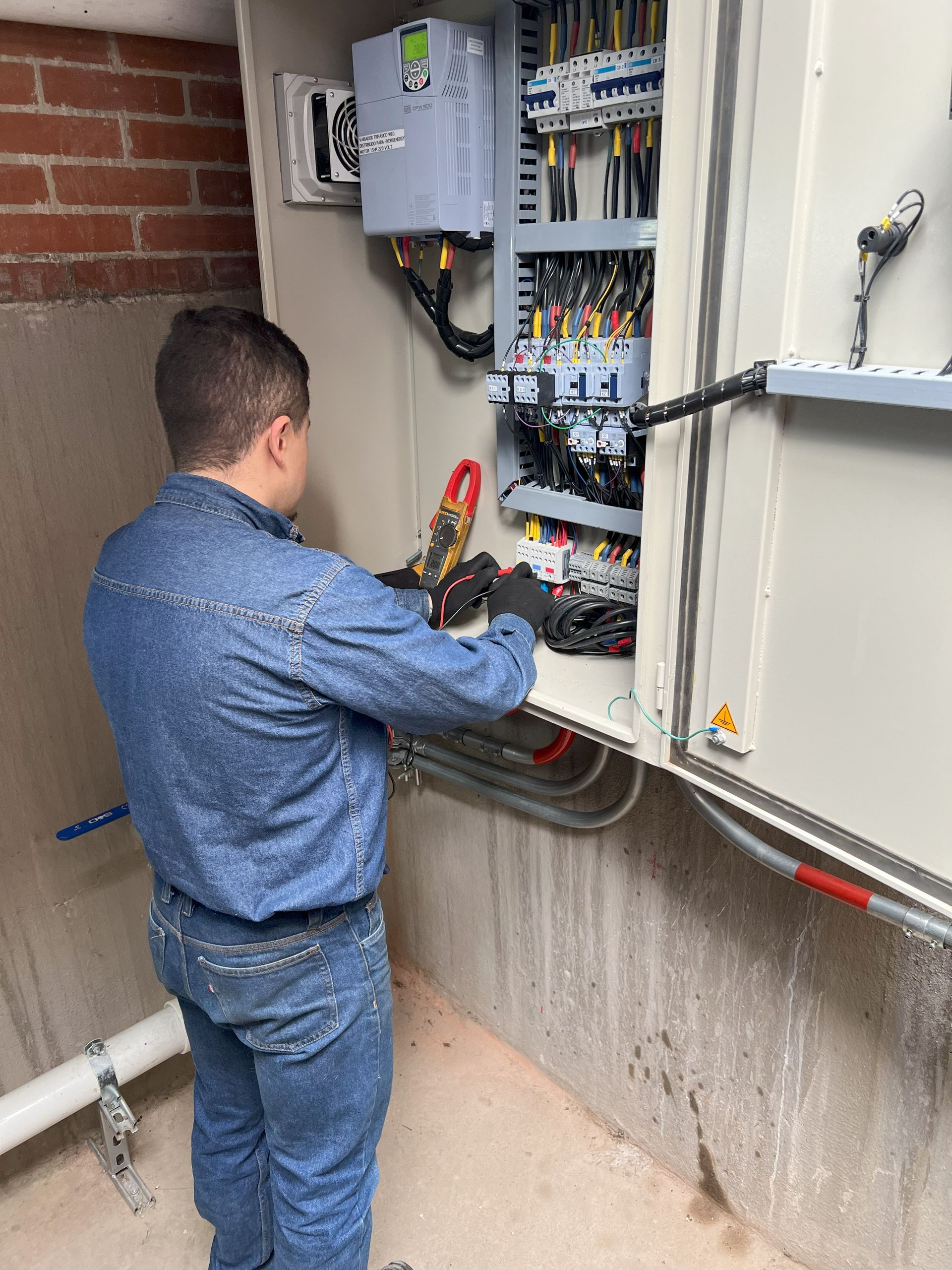 Hombre con chaqueta vaquera trabajando en un panel eléctrico dentro de un recinto de hormigón.