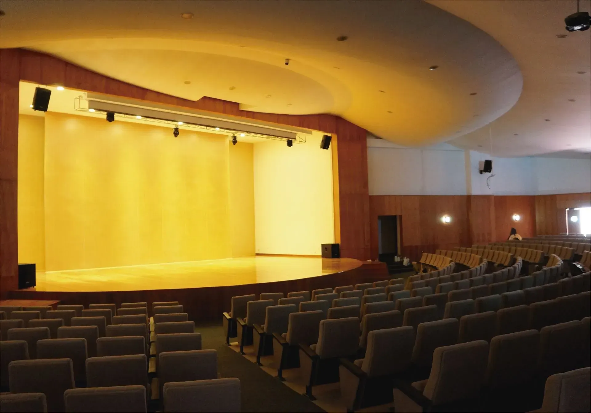 Auditorio con escenario iluminado en amarillo, filas de asientos y techo curvo.