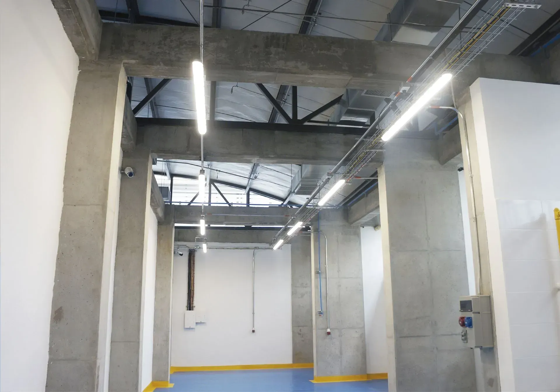 Columnas y vigas de hormigón que sostienen un techo con iluminación de tira; vista interior.