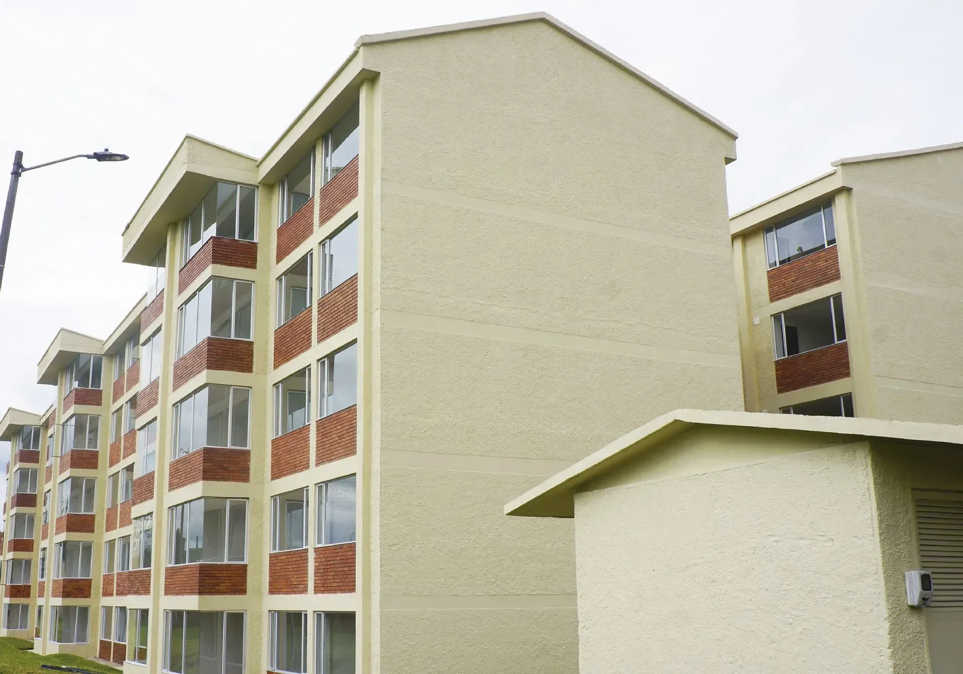 Edificio de apartamentos con fachada beige, de varios pisos, con detalles de ladrillo rojo alrededor de las ventanas.