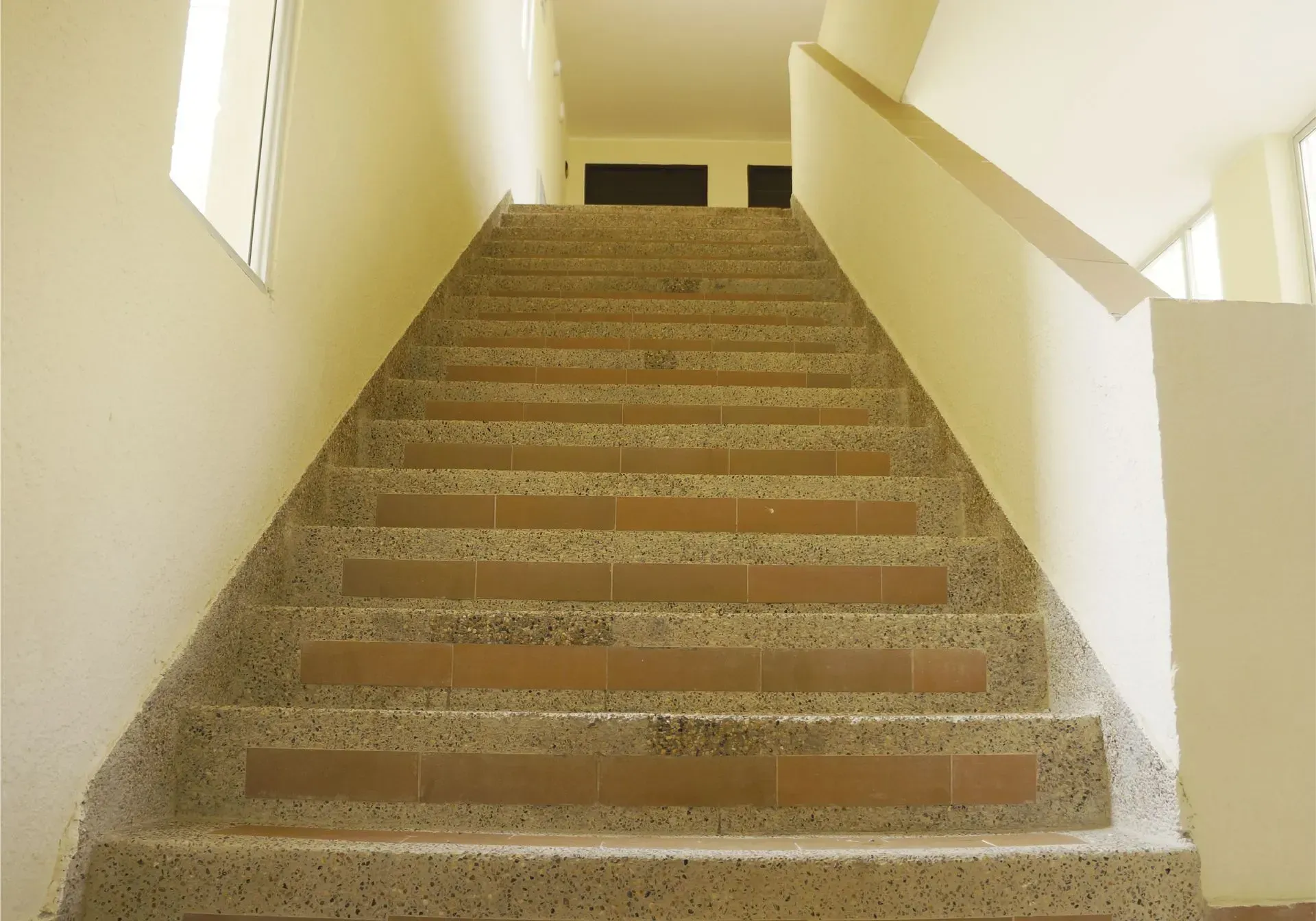 Escalera que sube hacia arriba con escalones y paredes de color beige y marrón.