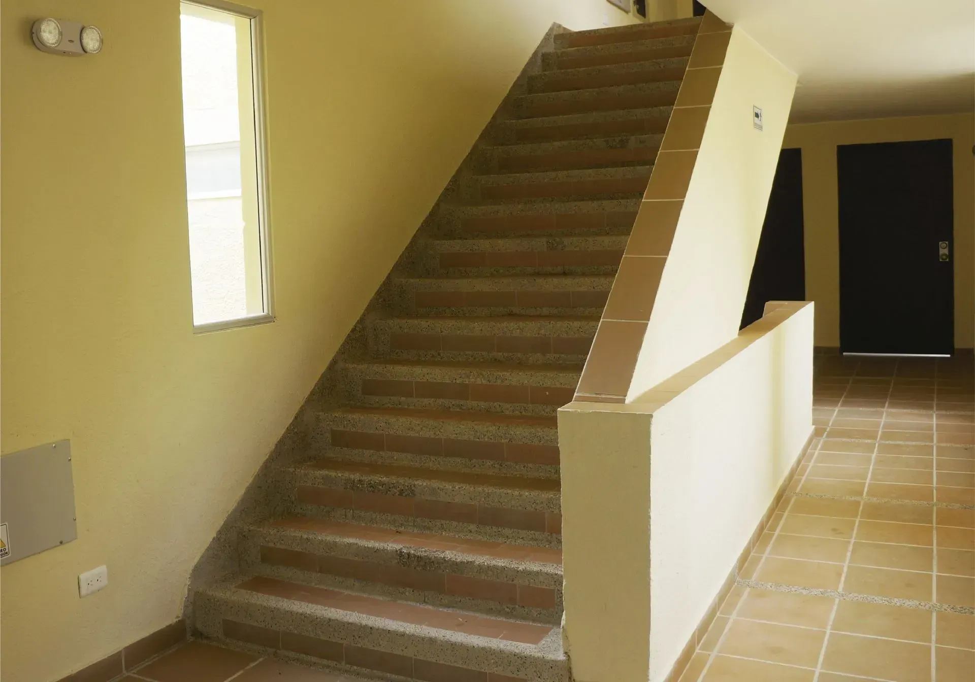Escalera en el pasillo del edificio con escalones de ladrillo marrón claro y paredes de color beige.