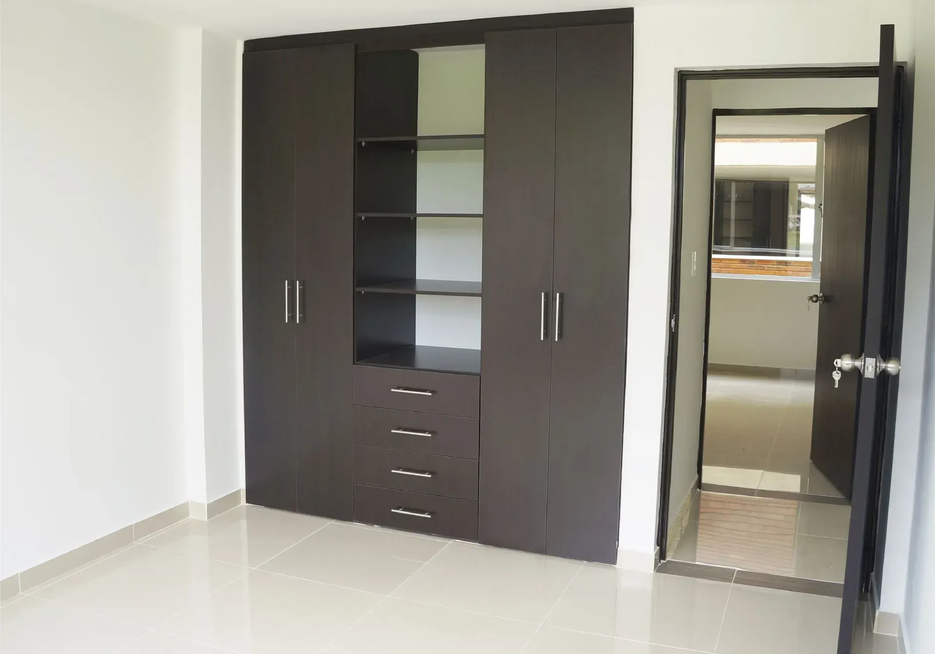 Armario de color marrón oscuro con puertas, estantes y cajones en una habitación con puerta abierta.