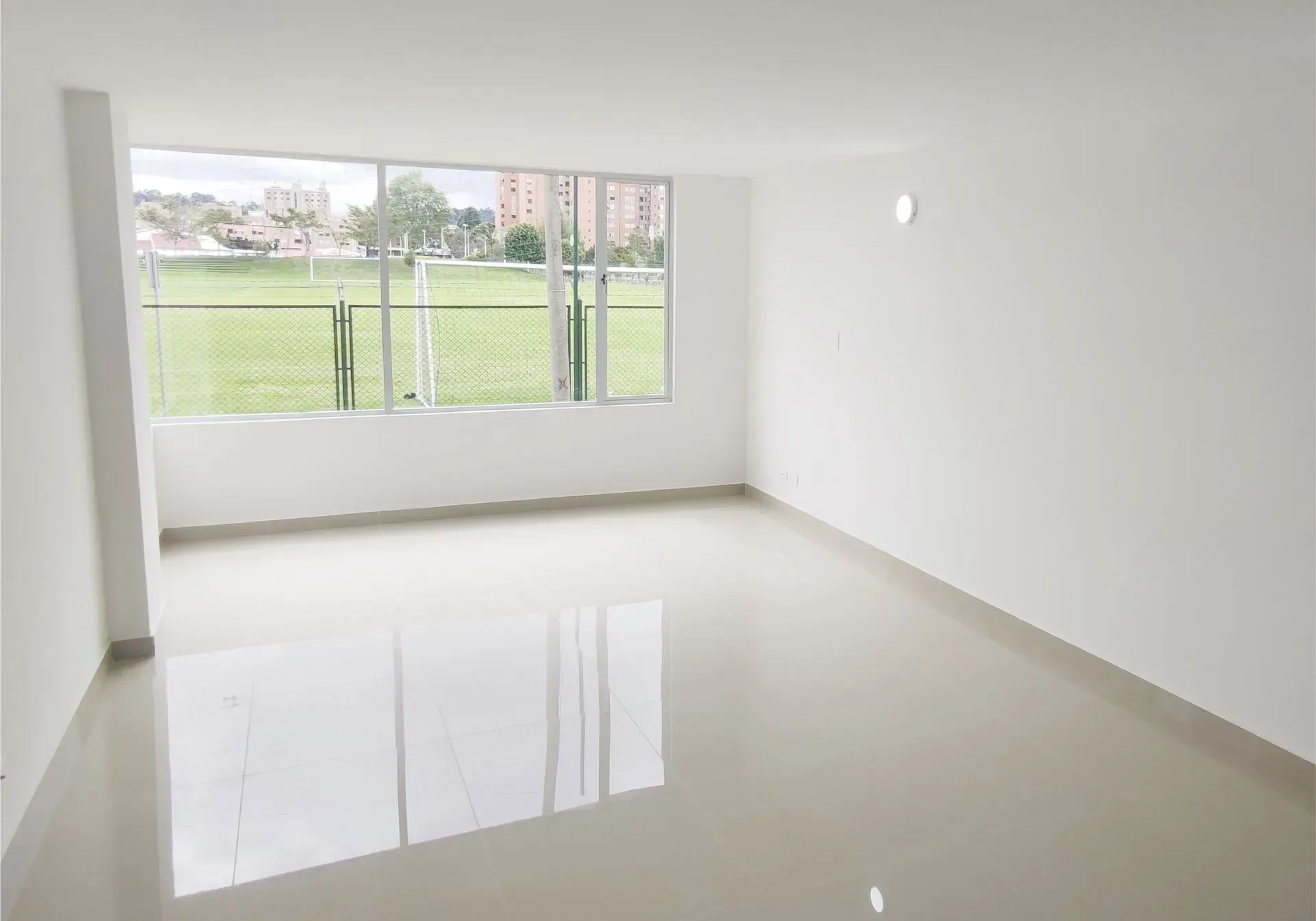 Habitación blanca vacía y luminosa con una gran ventana que da a un campo verde.