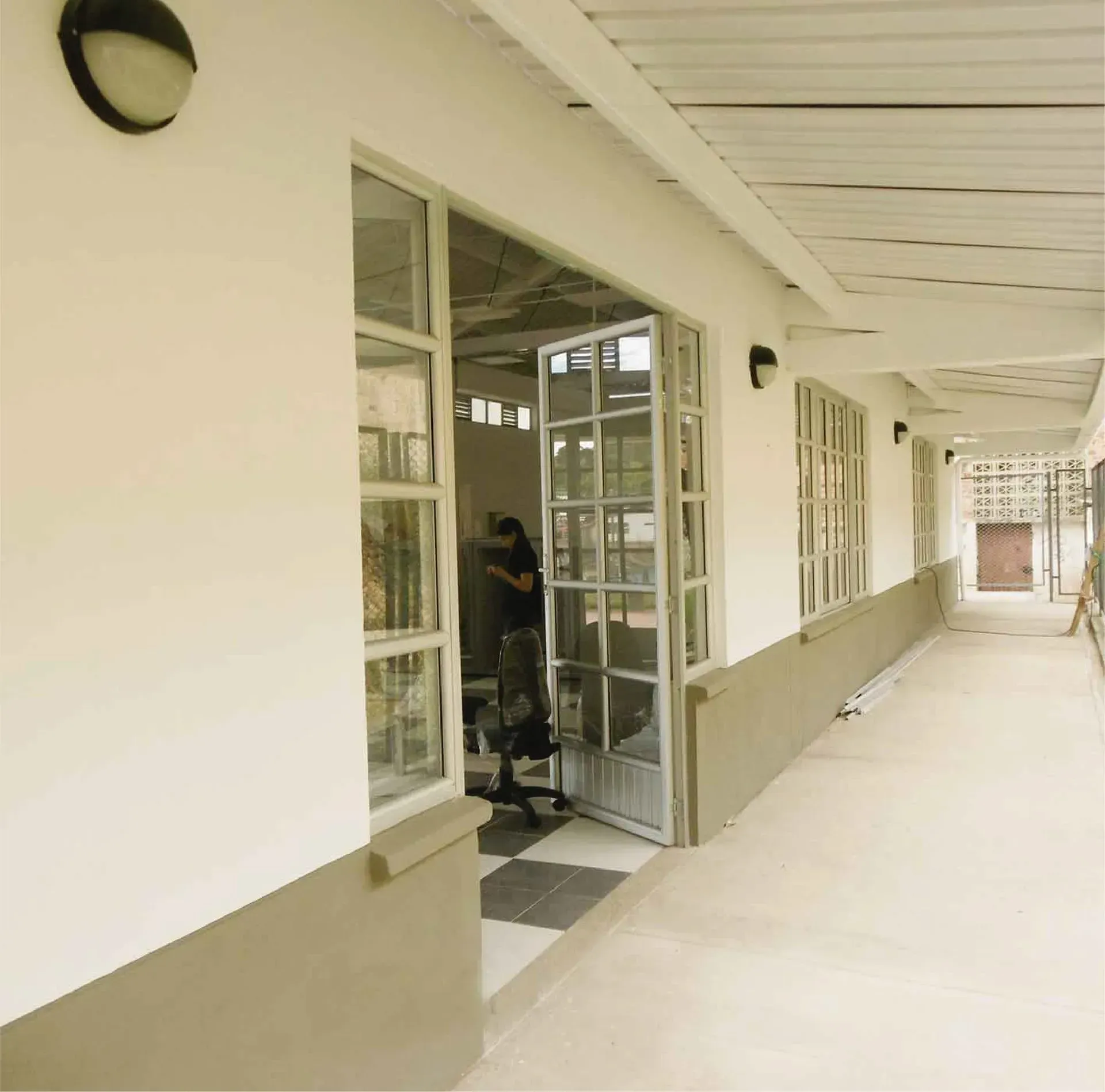 Vista exterior del edificio con paredes blancas, puerta abierta y pasillo largo.