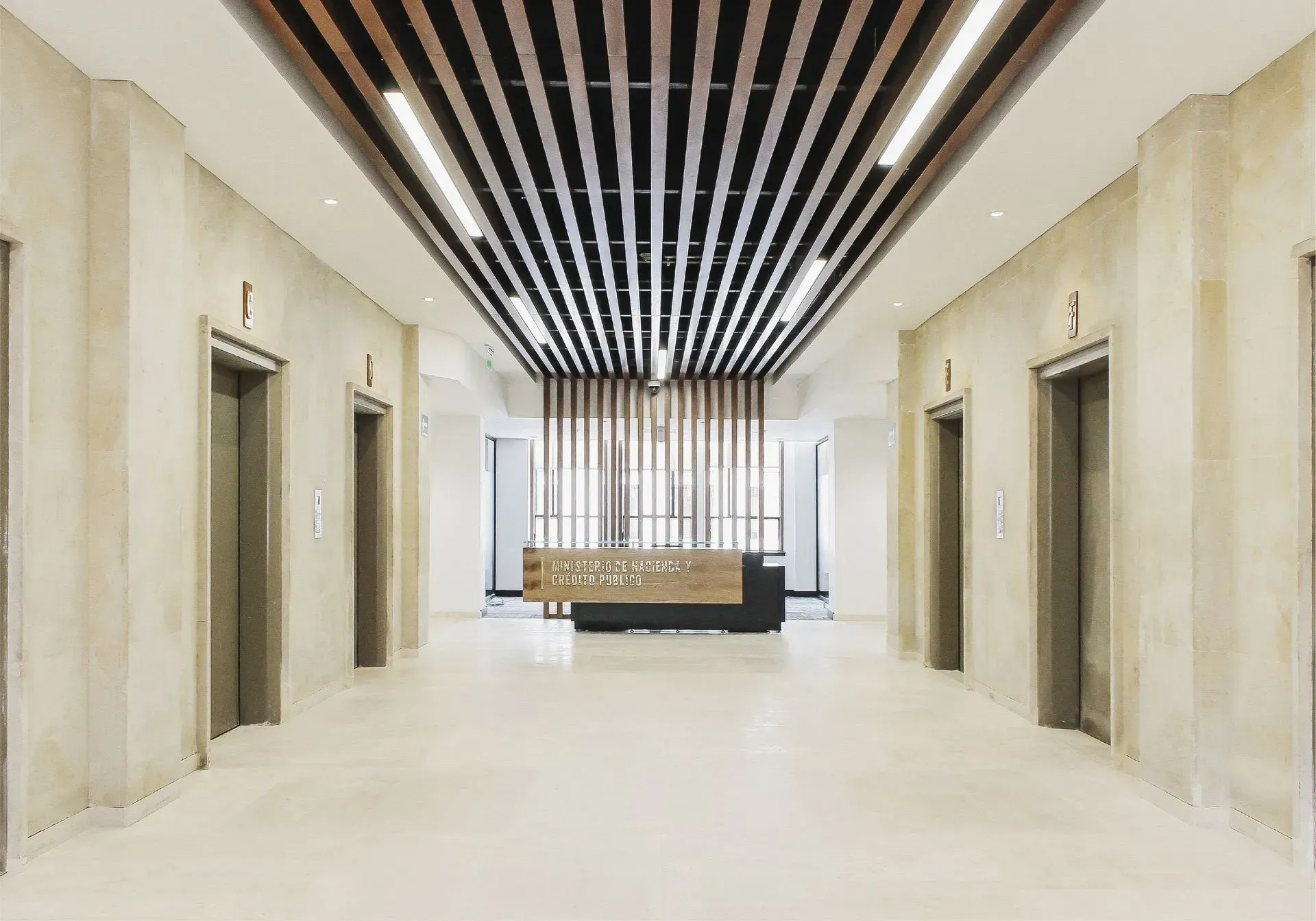 Vestíbulo con tres ascensores, detalles en madera y mostrador de recepción. Colores neutros y diseño elegante.