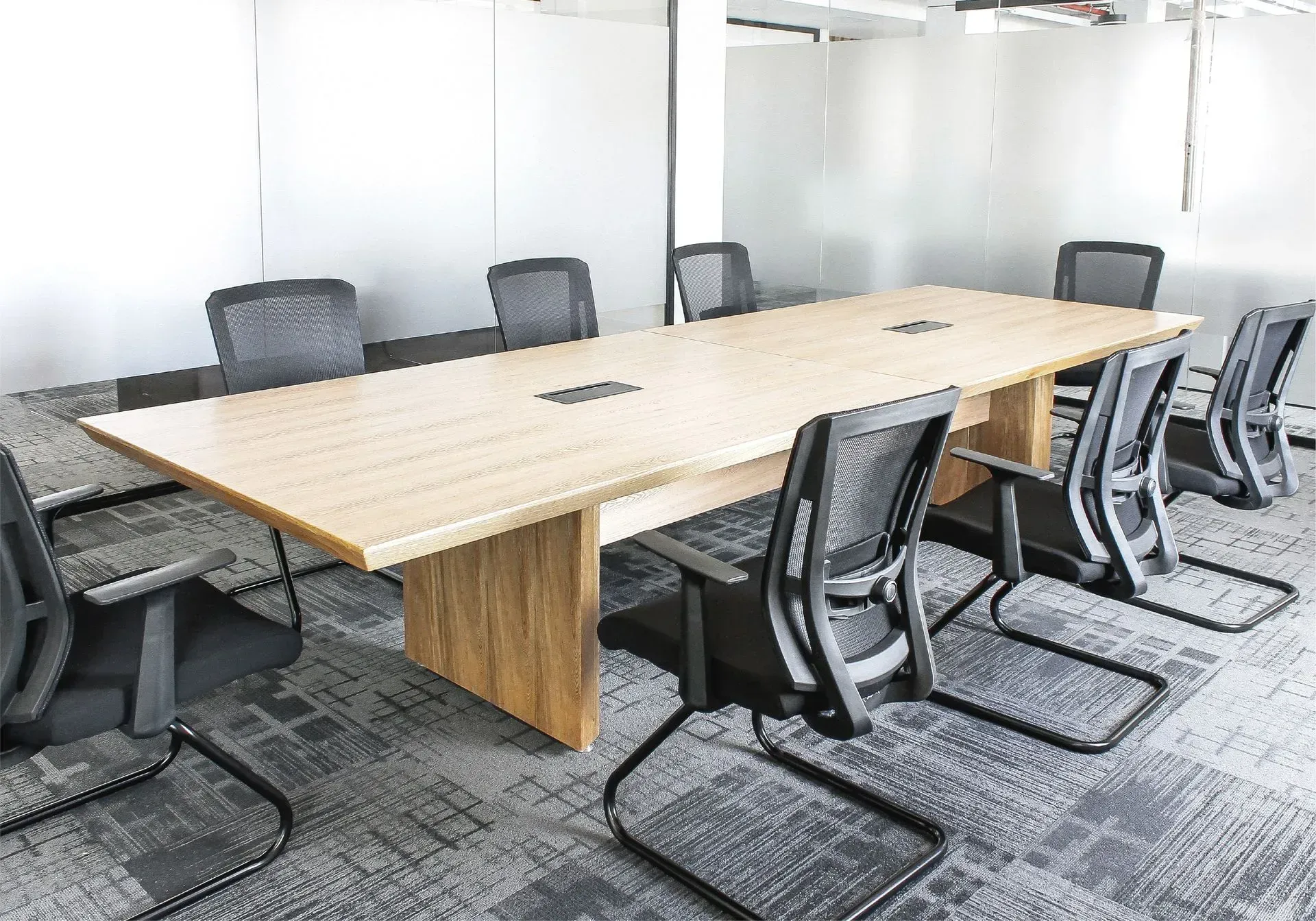 Sala de conferencias con mesa larga de madera y sillas negras, en un entorno de oficina.