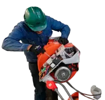 Persona con equipo de seguridad reparando máquina naranja, utilizando un destornillador.