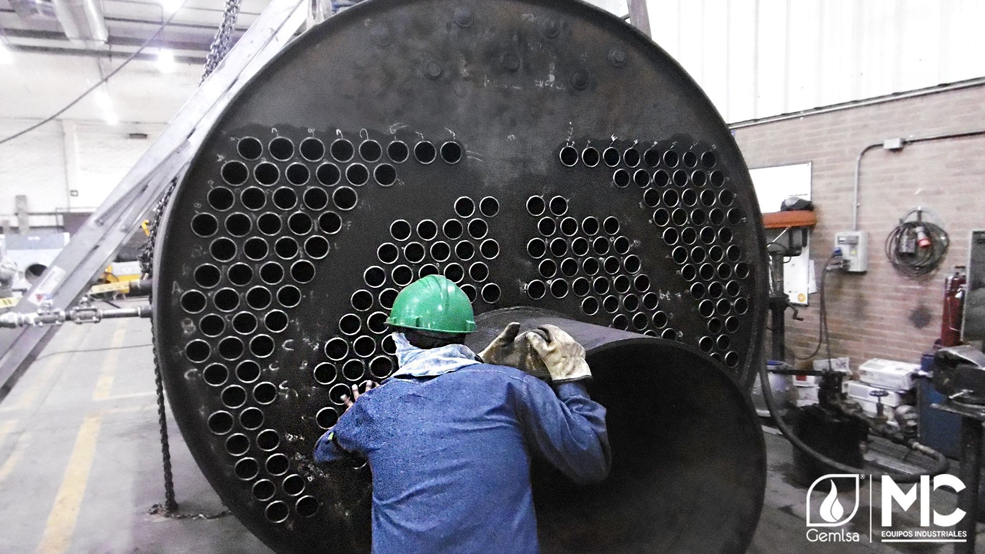 Hombre con equipo de protección trabajando en una gran estructura metálica con muchos agujeros, entorno industrial.