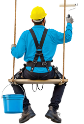 Pintor con casco amarillo y camisa azul pintando sentado en un columpio; cubo azul.