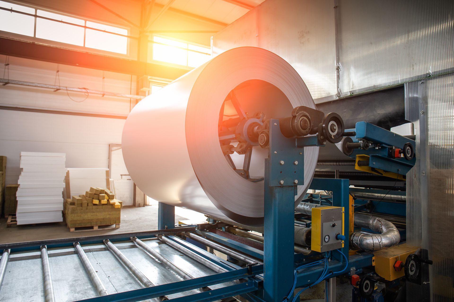 Large paper roll on industrial machinery in a factory, lit by warm sunlight.