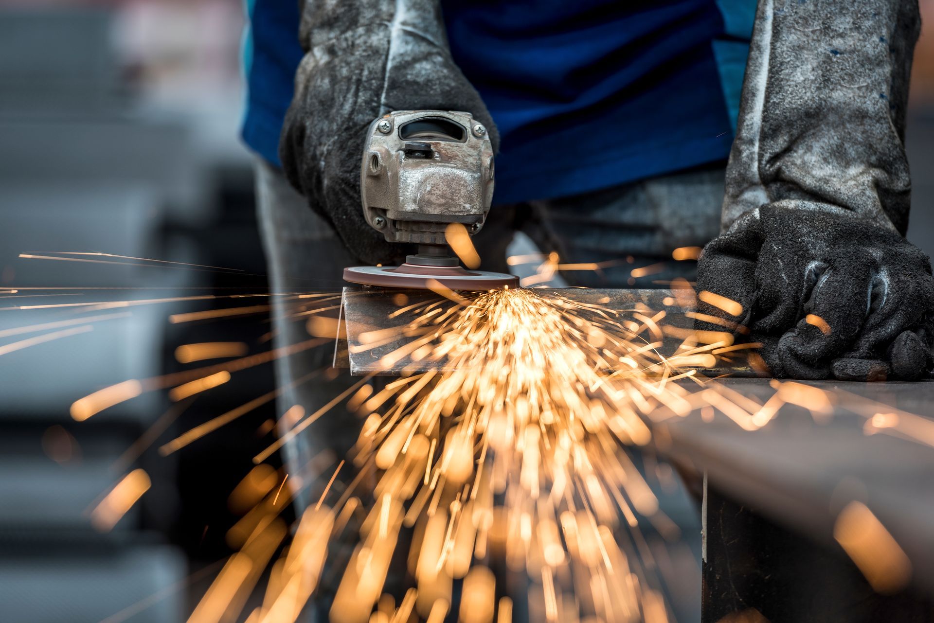 Gloved hands using an angle grinder to cut metal, with bright sparks flying.