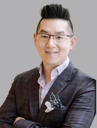 A man in a suit and glasses is leaning against a wall with his arms crossed.