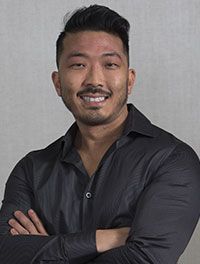 A man with a beard is wearing a black shirt and smiling with his arms crossed.