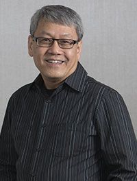 A man wearing glasses and a striped shirt is smiling for the camera.