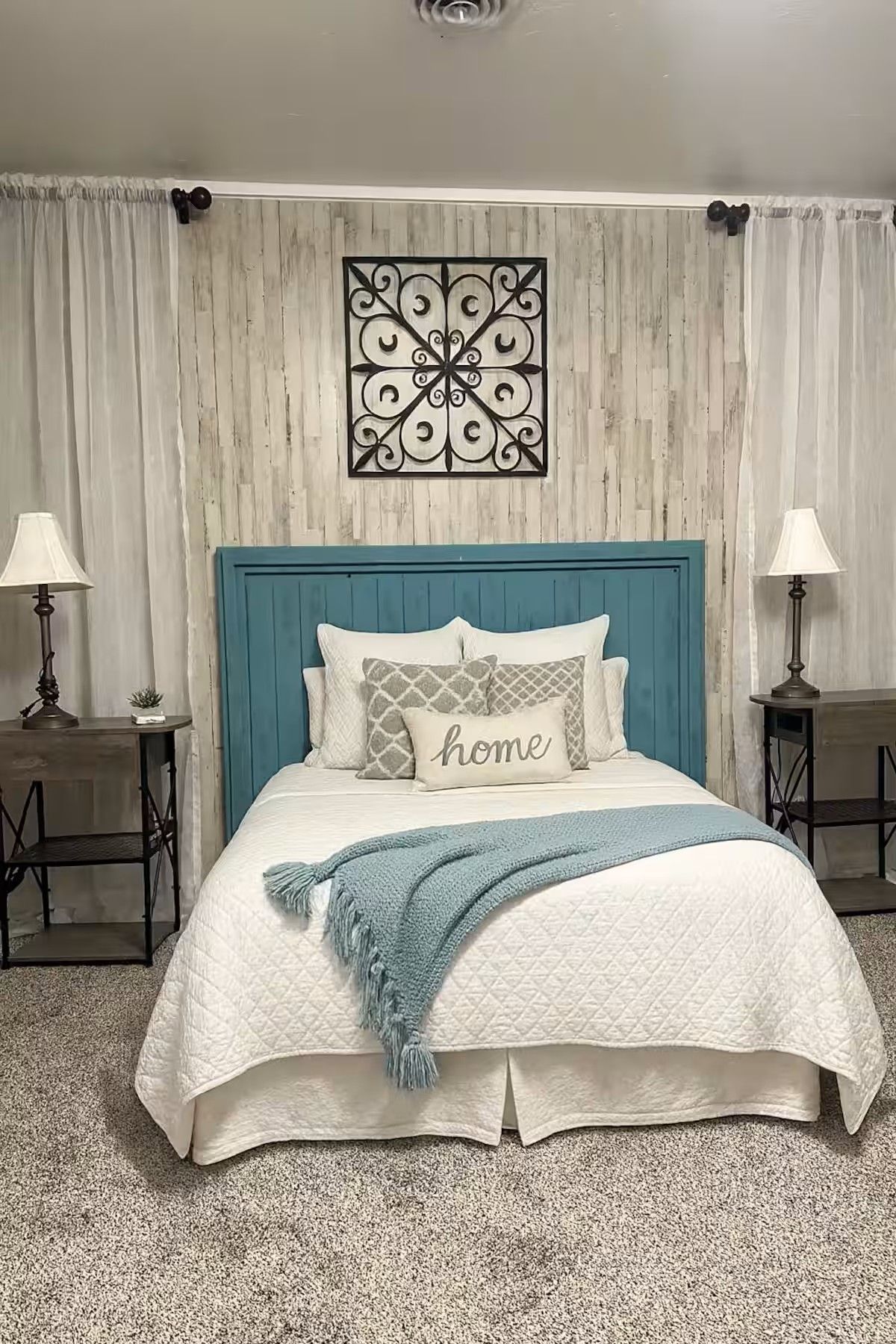 Bedroom with blue headboard, white bedding, and a light blue throw. Features wood wall and decorative metal piece.