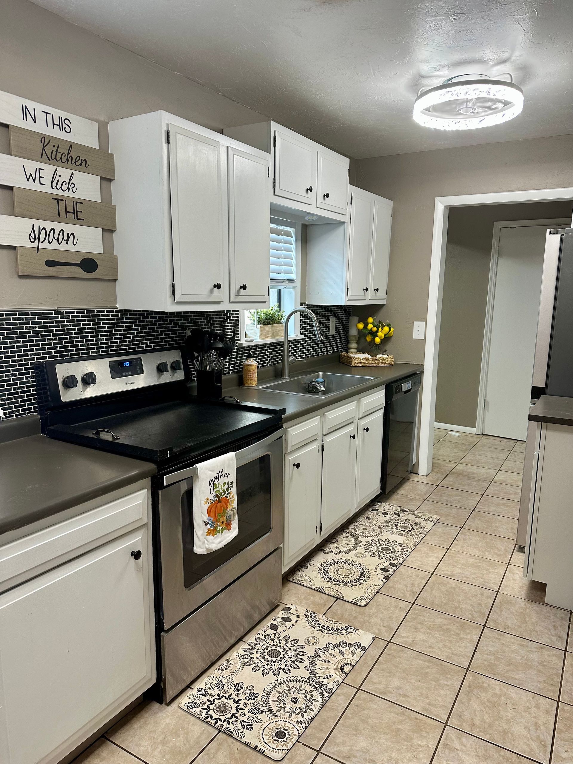 White kitchen with stainless steel appliances, dark countertops, and patterned backsplash.