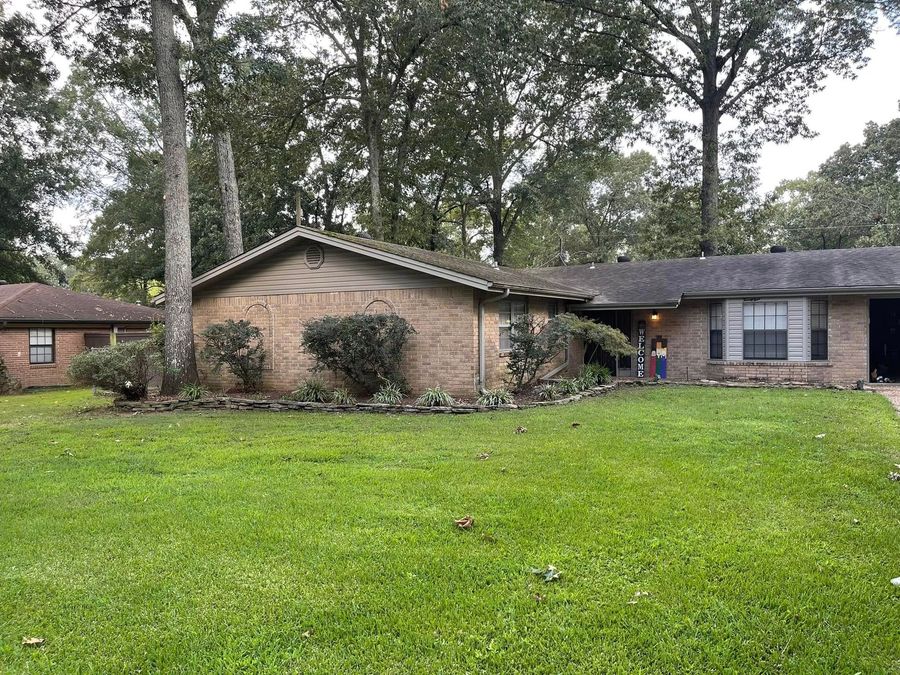 Modern house with large windows and a green lawn, bordered by shrubs under warm sunlight