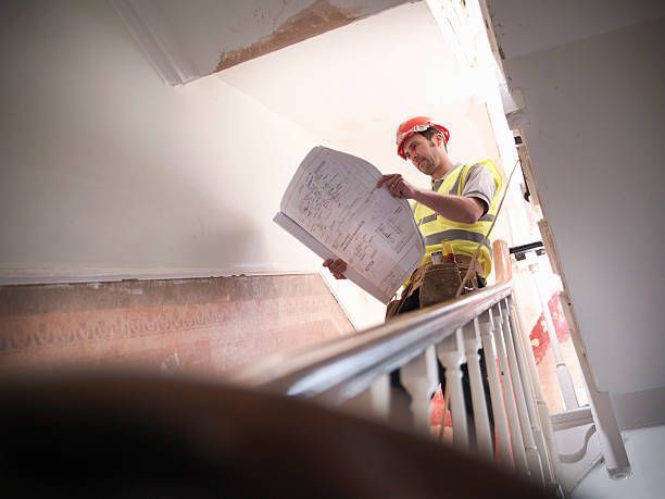 Construction worker on stairs examines blueprints in a building under renovation.