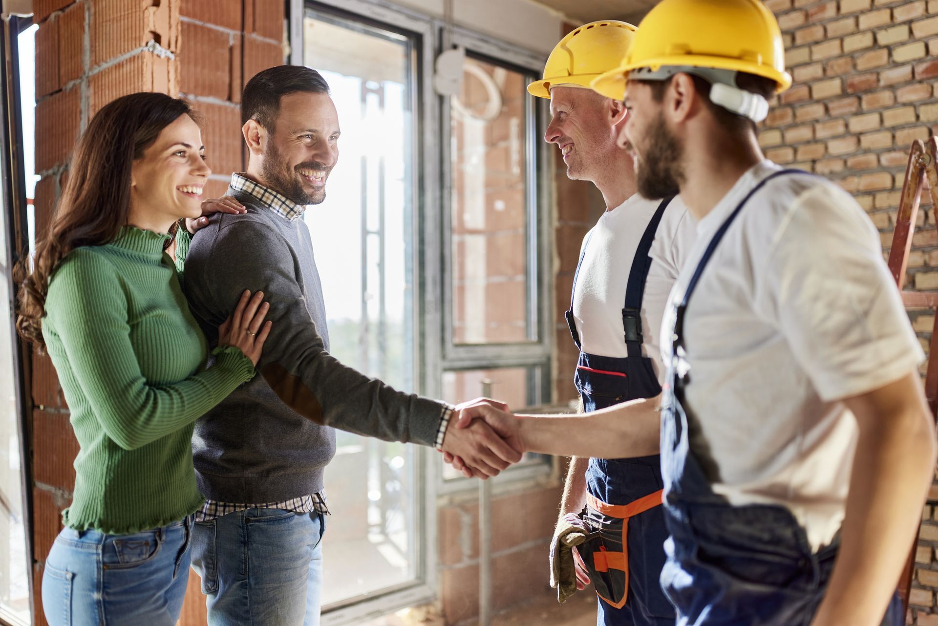 Couple shaking hands with construction workers at a construction site.