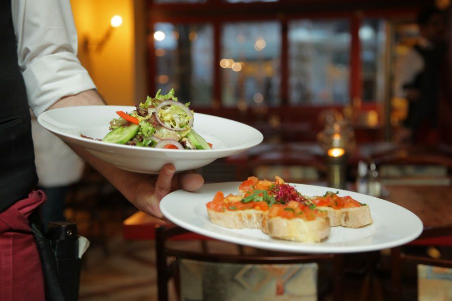 A server holding a plate of salad and a plate of bruschetta in a restaurant setting.
