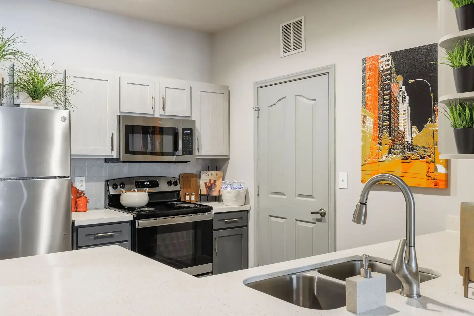 Kitchen with stainless steel appliances, gray cabinets, white countertop, and artwork.