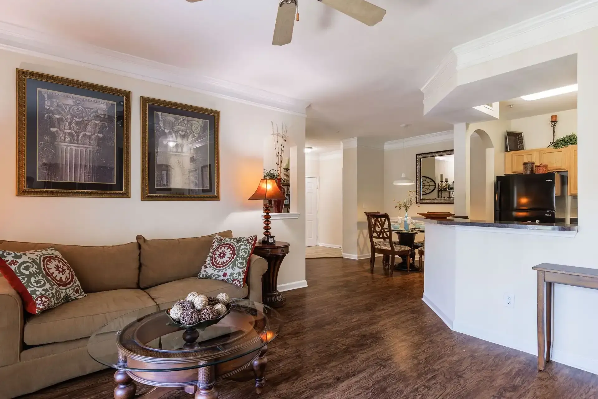 Living room with brown couch, artwork, and view into the kitchen and dining area.