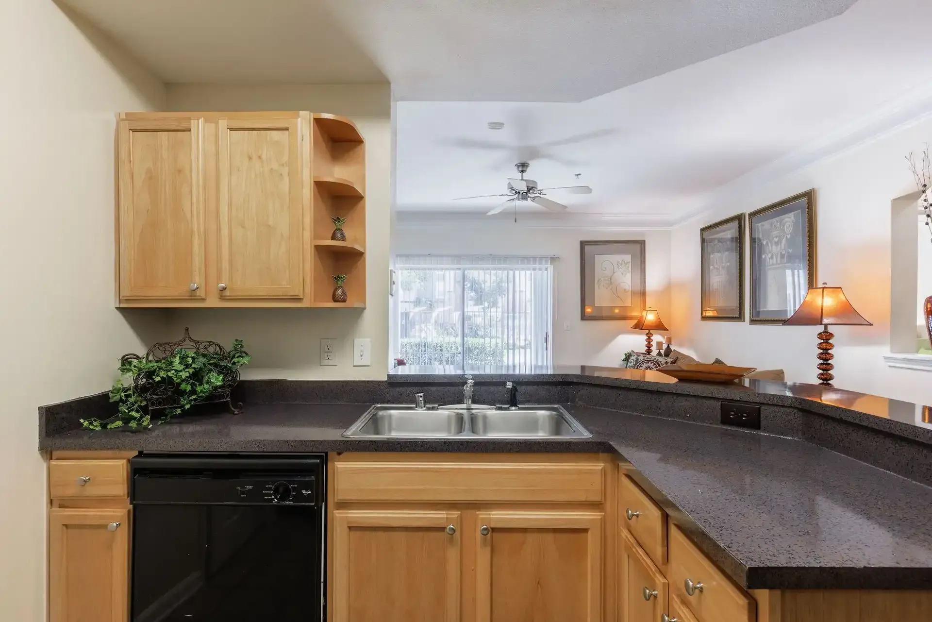 Kitchen with brown countertops, wooden cabinets, and a sink; view into a living area.