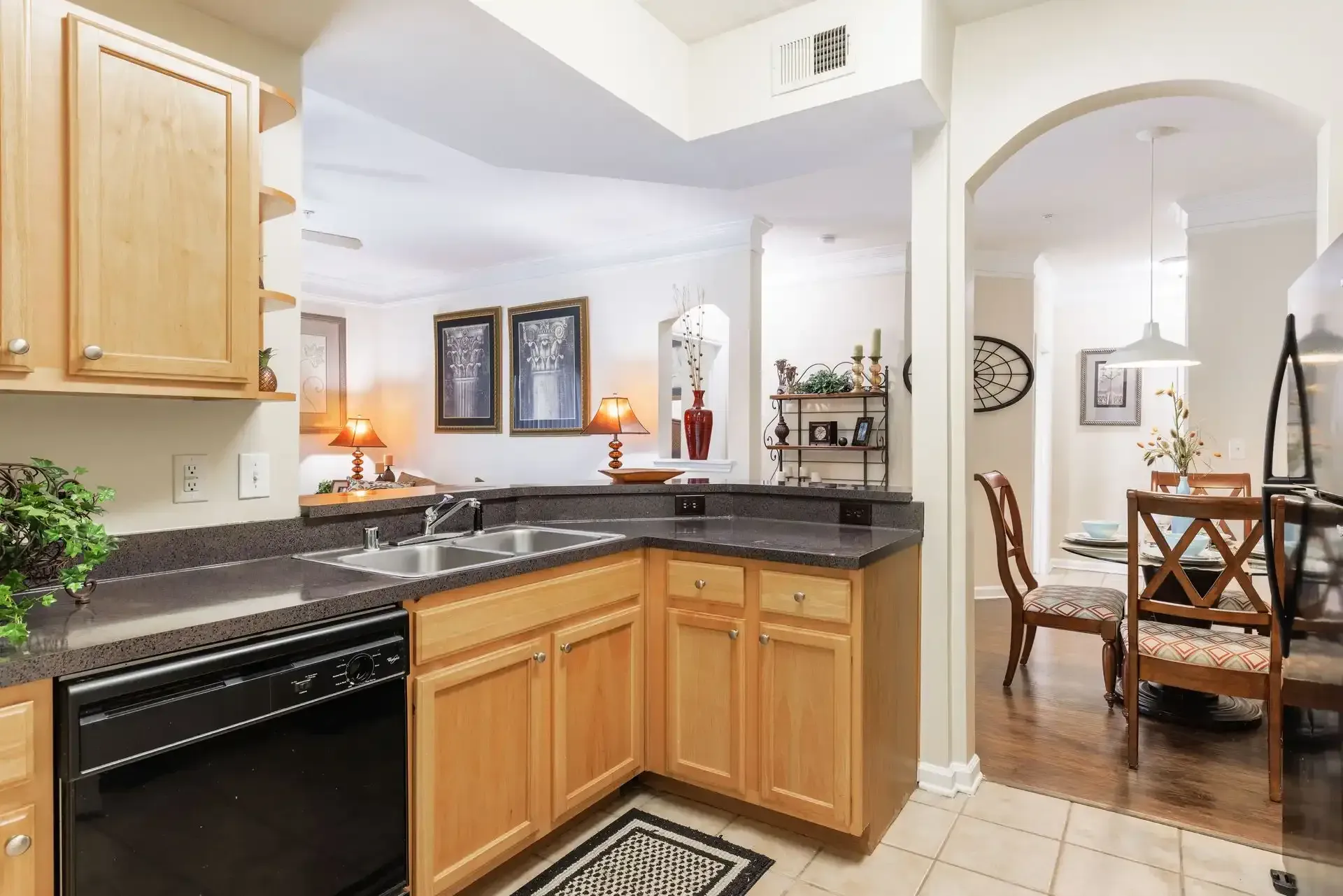 Kitchen with wooden cabinets, black appliances, and a view into a dining area through an arched doorway.