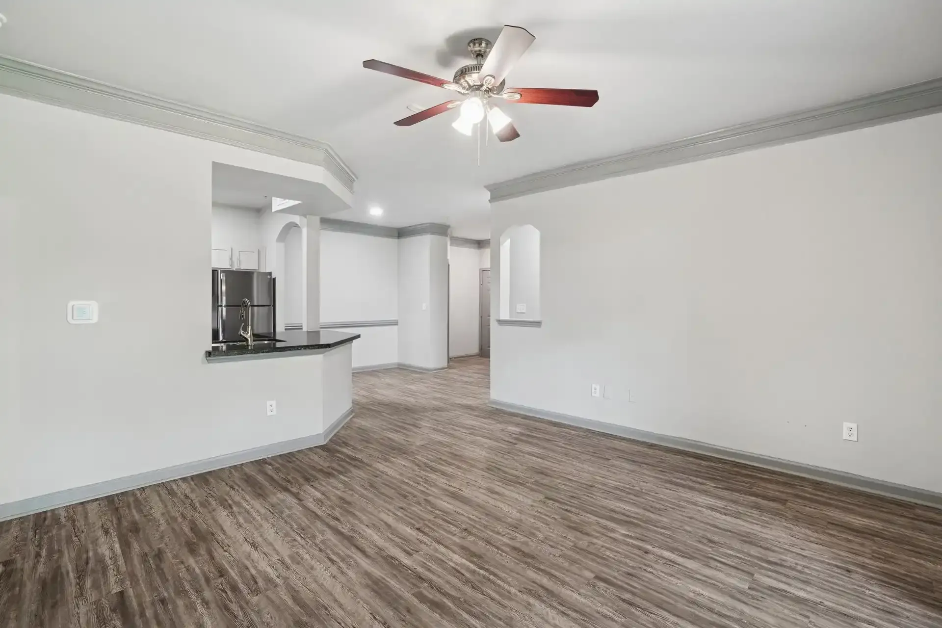 Spacious living area with wood-look flooring, gray walls, and a ceiling fan.