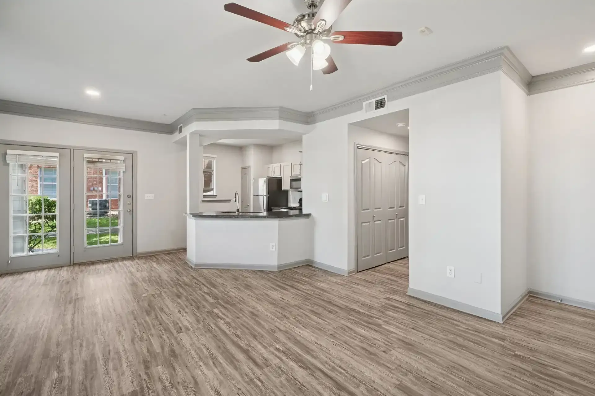 Living room with French doors, kitchen, and wood-look flooring. White walls, gray trim, and ceiling fan.