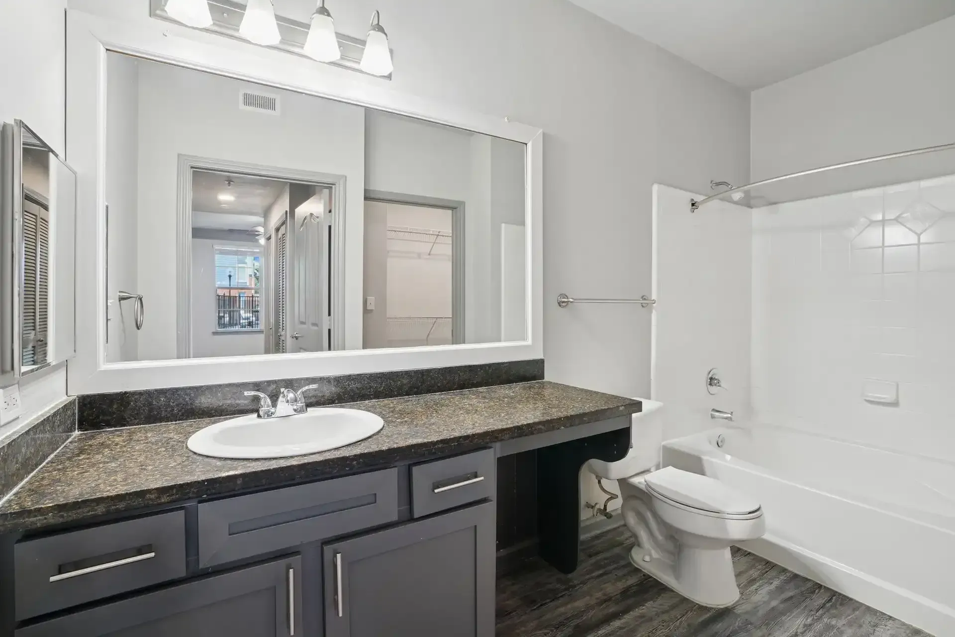 Bathroom with gray cabinets, dark countertop, white sink, and tub.